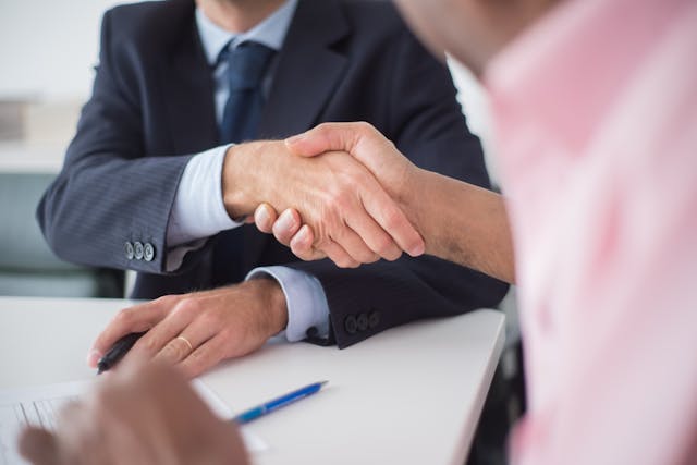 Person wearing a suit shaking hands with someone in a pink shirt